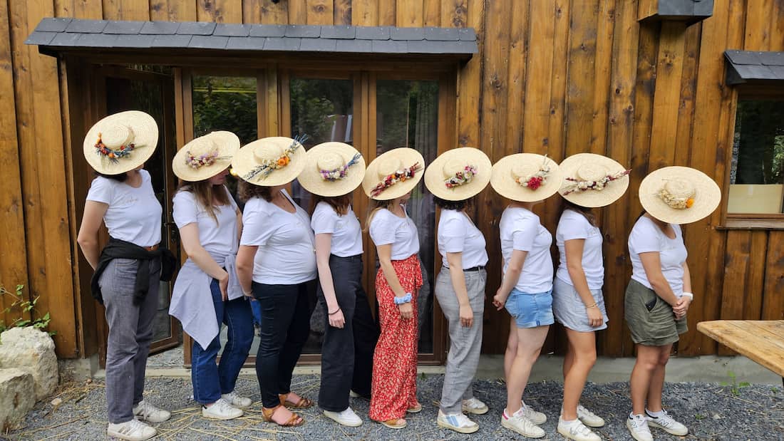 photo d'un groupe EVJF de Deauville avec leurs chapeaux fleuris suite à l'atelier fleurs séchées à la ferme devant le séchoir. Prêtes pour le mariage