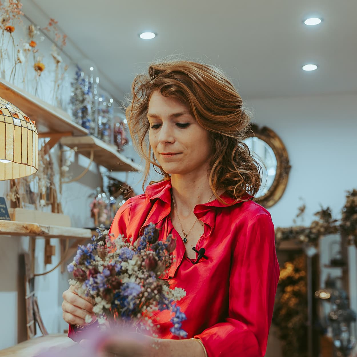 Charlotte, artisan créateur, compose un bouquet de fleurs séchées dans l'atelier. Savoir-faire manuel d'excellence et geste précis.