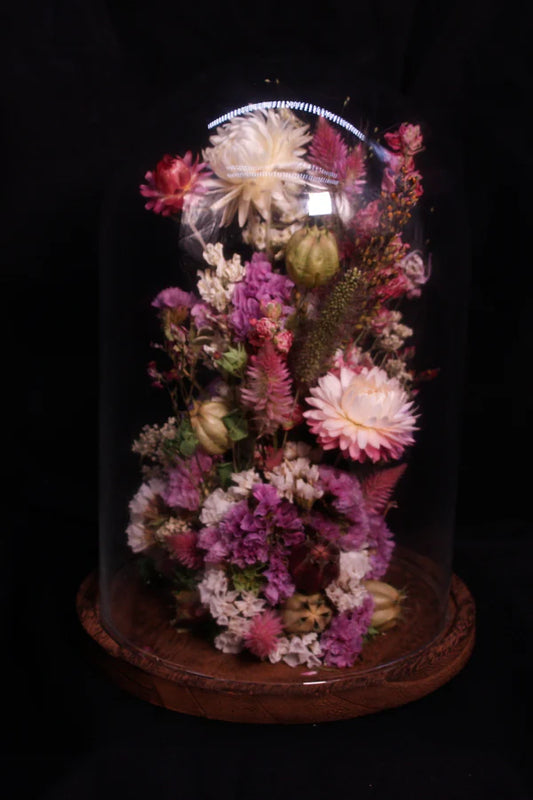 Grande cloche de fleurs séchées présentée sur un socle en bois foncé élégant.