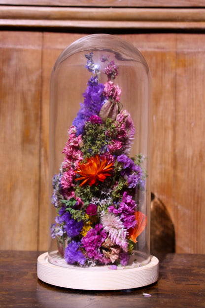 Cloche en verre protégeant des fleurs éternelles aux couleurs douces et naturelles.