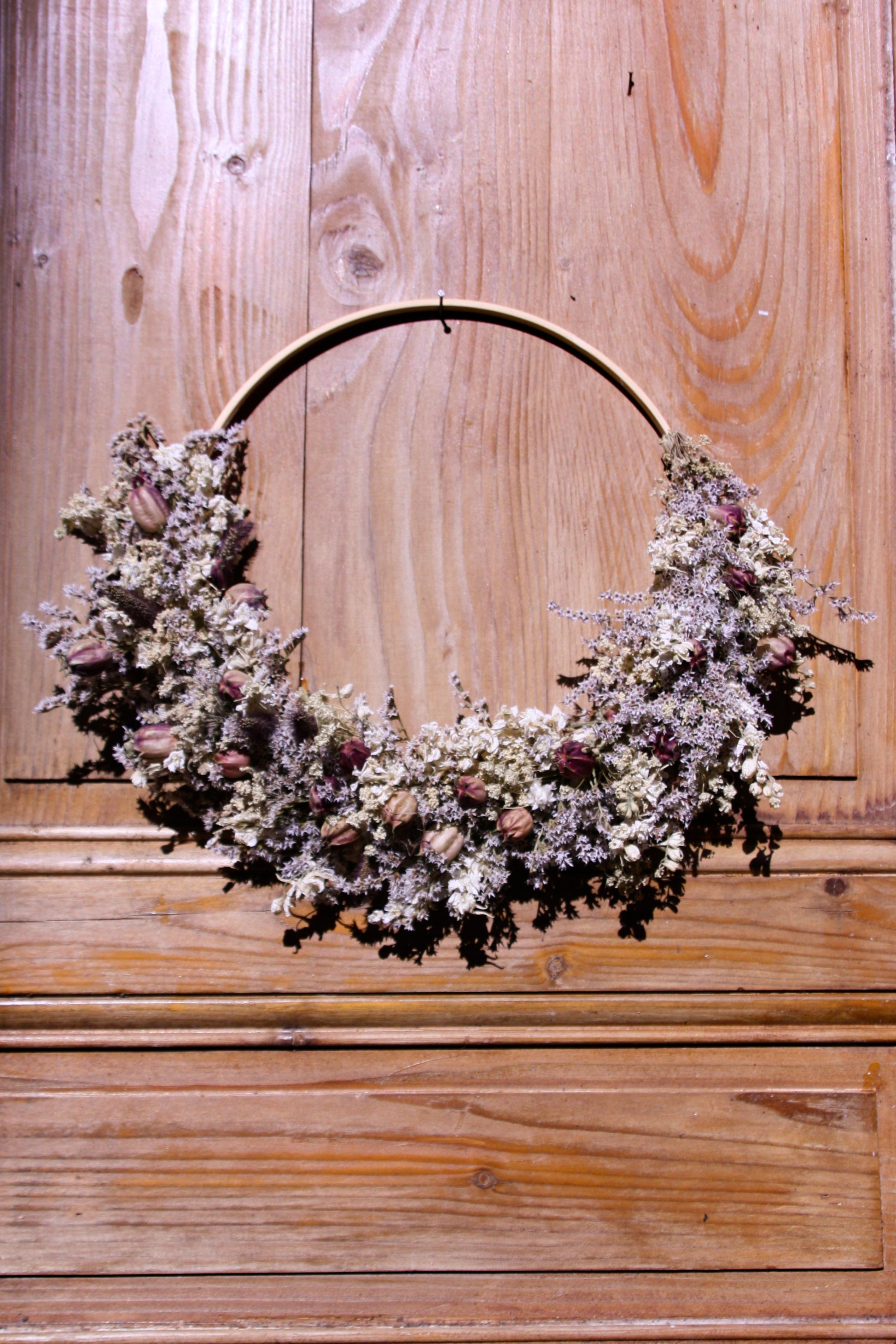 Couronne murale en fleurs séchées naturelles tressée en demi-lune sur un cercle en bois. Création artisanale aux tons blanc