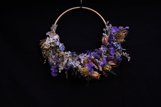 Couronne murale en fleurs séchées naturelles tressée en demi-lune sur un cercle en bois. Création artisanale aux tons bleus