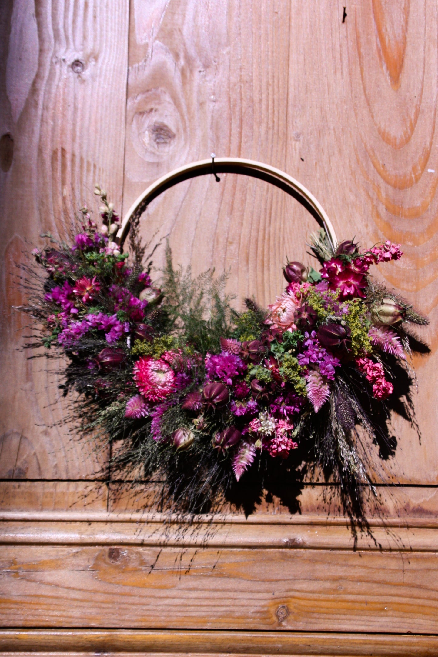 Couronne murale en fleurs séchées naturelles tressée en demi-lune sur un cercle en bois. Création artisanale aux tons roses