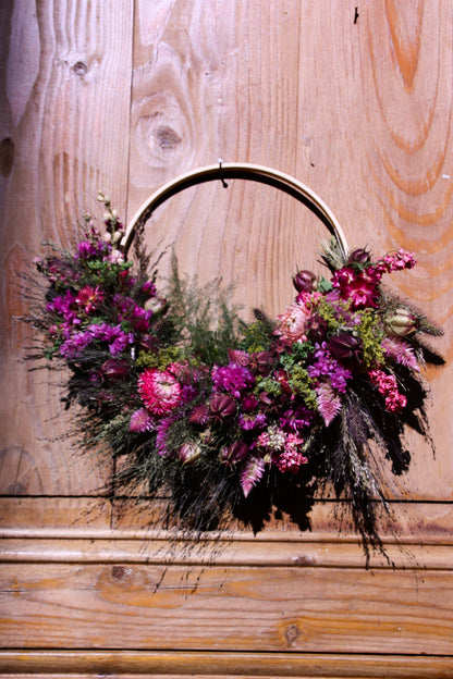 Couronne murale en fleurs séchées naturelles tressée en demi-lune sur un cercle en bois. Création artisanale aux tons roses