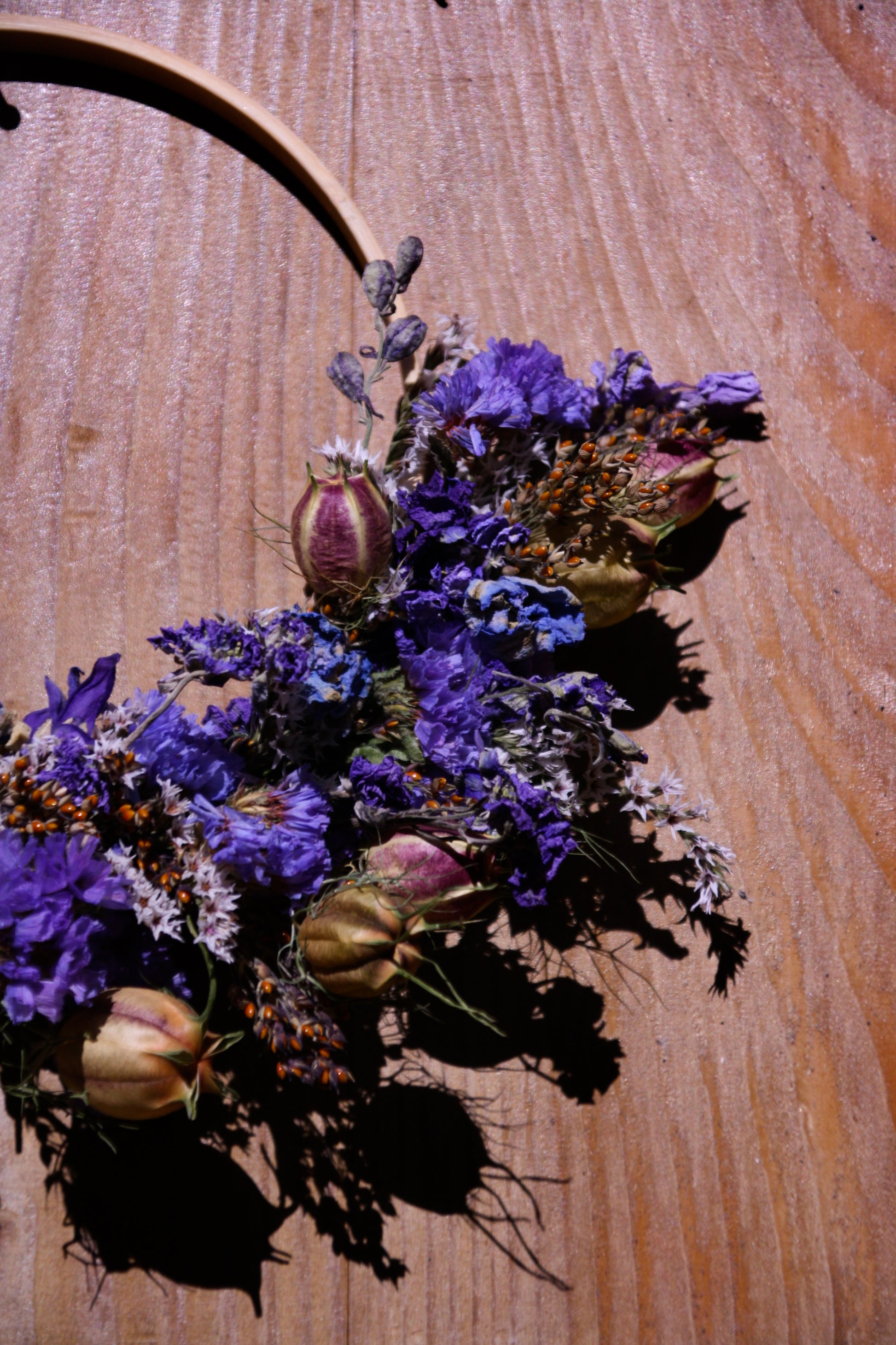 Couronne murale en fleurs séchées naturelles tressée en demi-lune sur un cercle en bois. Création artisanale aux tons bleus