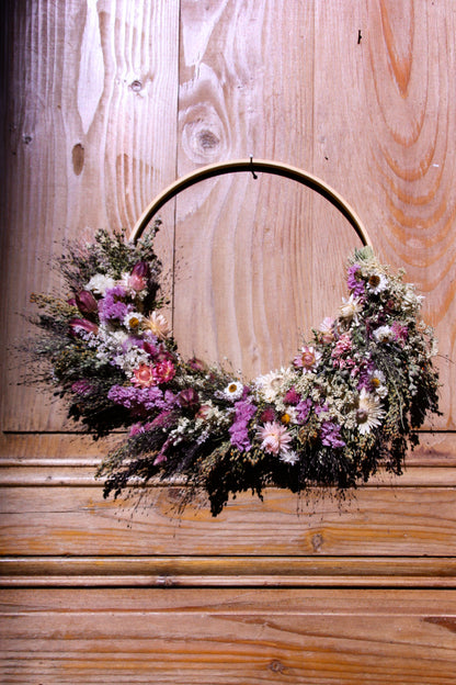 Couronne murale en fleurs séchées naturelles tressée en demi-lune sur un cercle en bois. Création artisanale aux tons roses et blancs