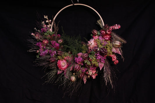 Couronne murale en fleurs séchées naturelles tressée en demi-lune sur un cercle en bois. Création artisanale aux tons roses