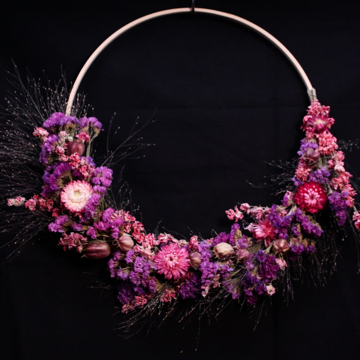 Couronne murale en fleurs séchées nuances rose et violet sur cercle doré, décoration murale style bohème chic.