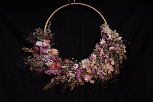 Couronne murale en fleurs séchées naturelles tressée en demi-lune sur un cercle en bois. Création artisanale aux tons roses et blancs