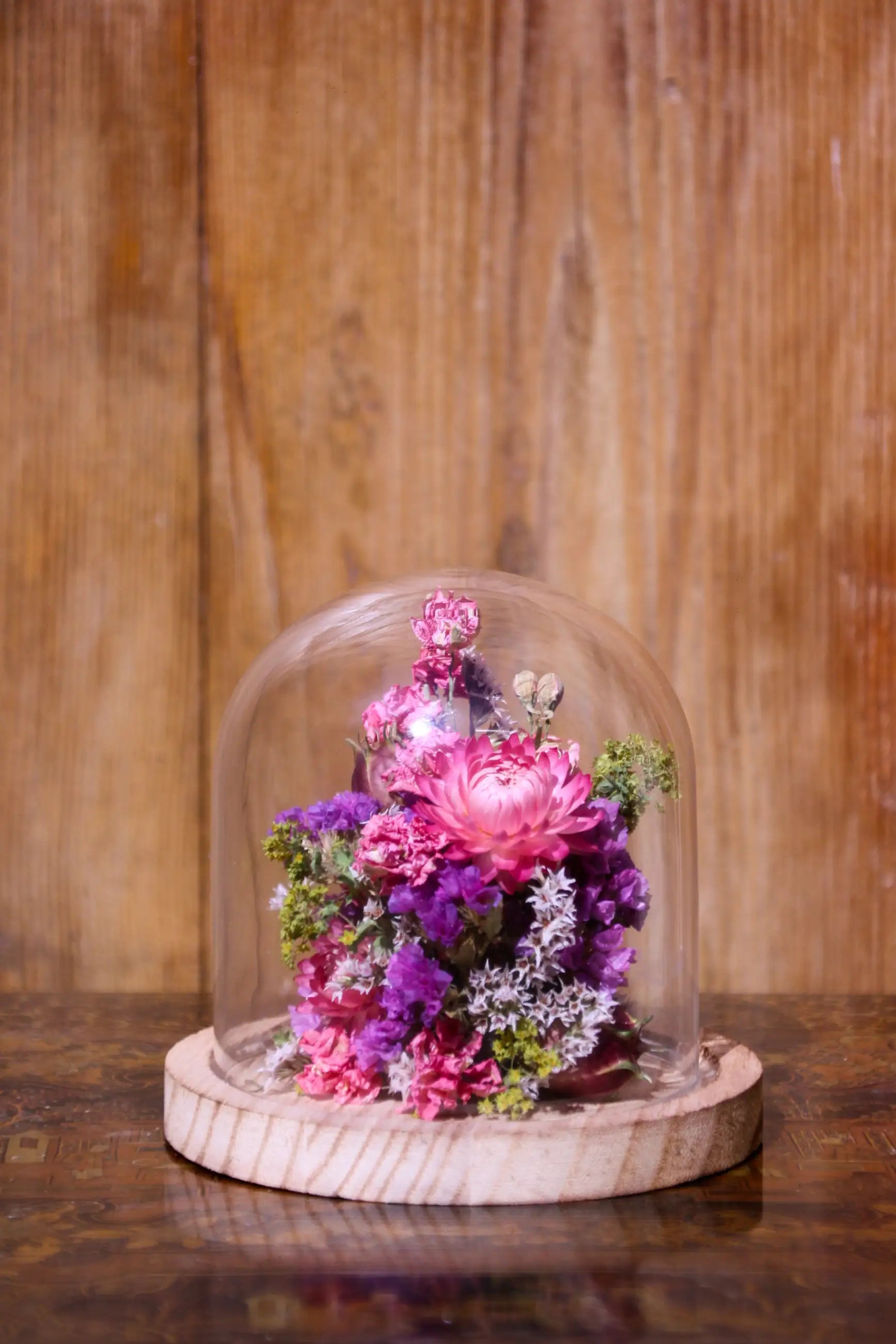 Création florale artisanale sous cloche avec un élégant socle en bois noir.