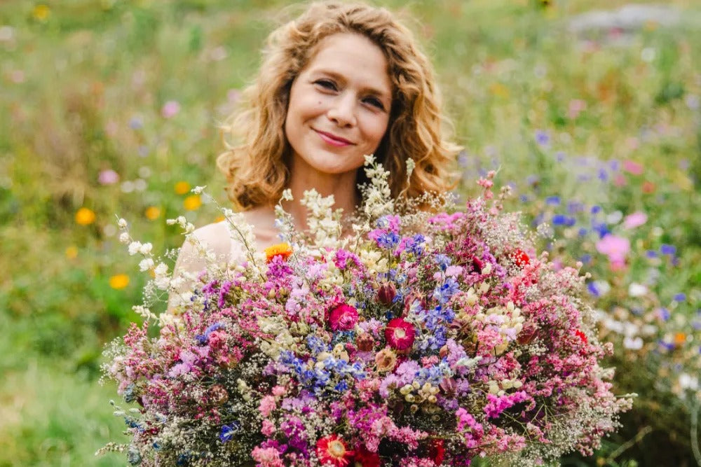 Portrait de Charlotte Co-fondatrice de la ferme florale des Fleurs de la Clarté en Normandie, tenant un bouquet dans ses mains au milieu des champs de fleurs