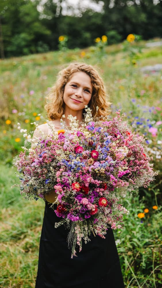 Portrait de Charlotte Co-fondatrice de la ferme florale des Fleurs de la Clarté en Normandie, tenant un bouquet dans ses mains au milieu des champs de fleurs