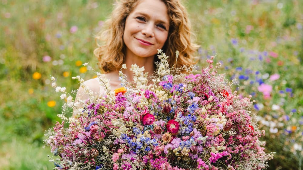 Portrait de Charlotte Co-fondatrice de la ferme florale des Fleurs de la Clarté en Normandie, tenant un bouquet dans ses mains au milieu des champs de fleurs