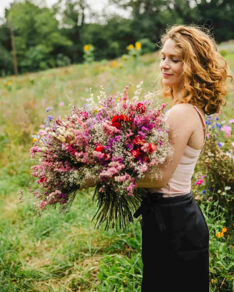 Productrice de fleurs séchées tenant un bouquet XXL coloré dans sa ferme florale en Normandie. Création artisanale d'exception.