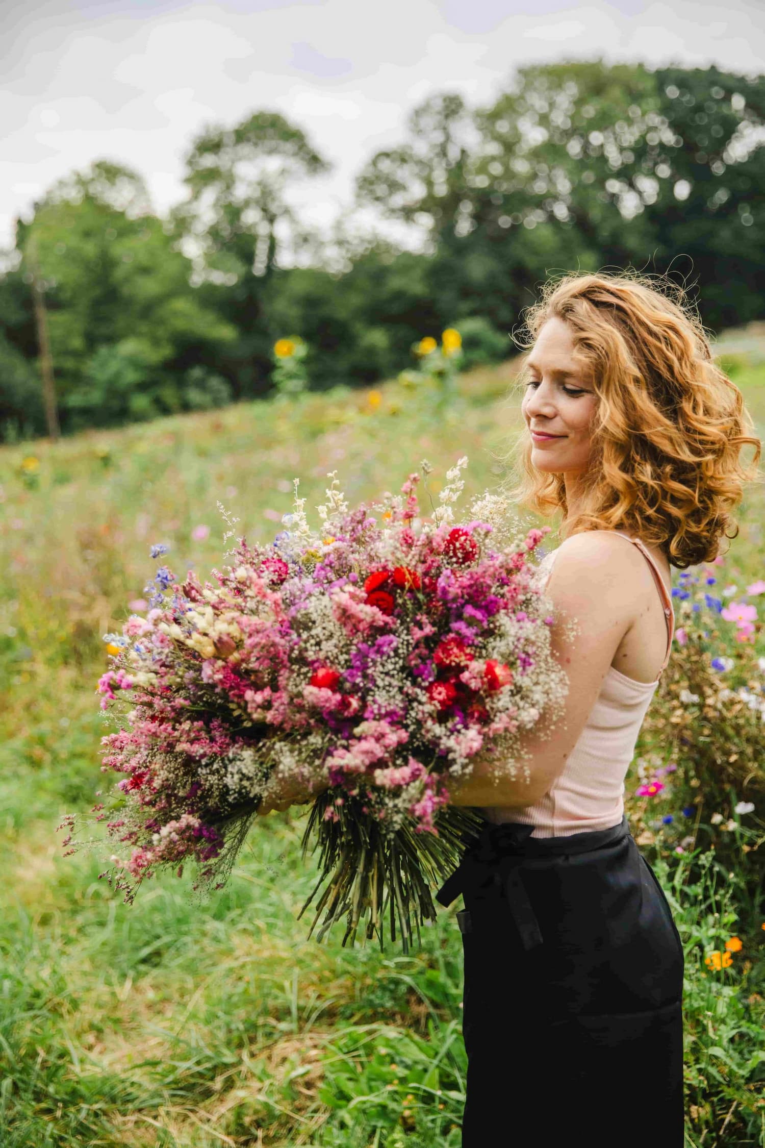 Productrice de fleurs séchées tenant un bouquet XXL coloré dans sa ferme florale en Normandie. Création artisanale d'exception.